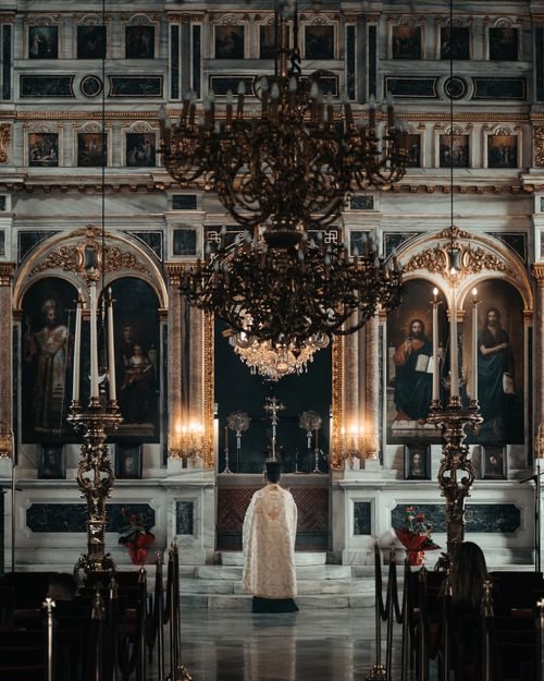 Free A priest kneels in a grand church in Istanbul, surrounded by ornate decor and chandeliers. Stock Photo