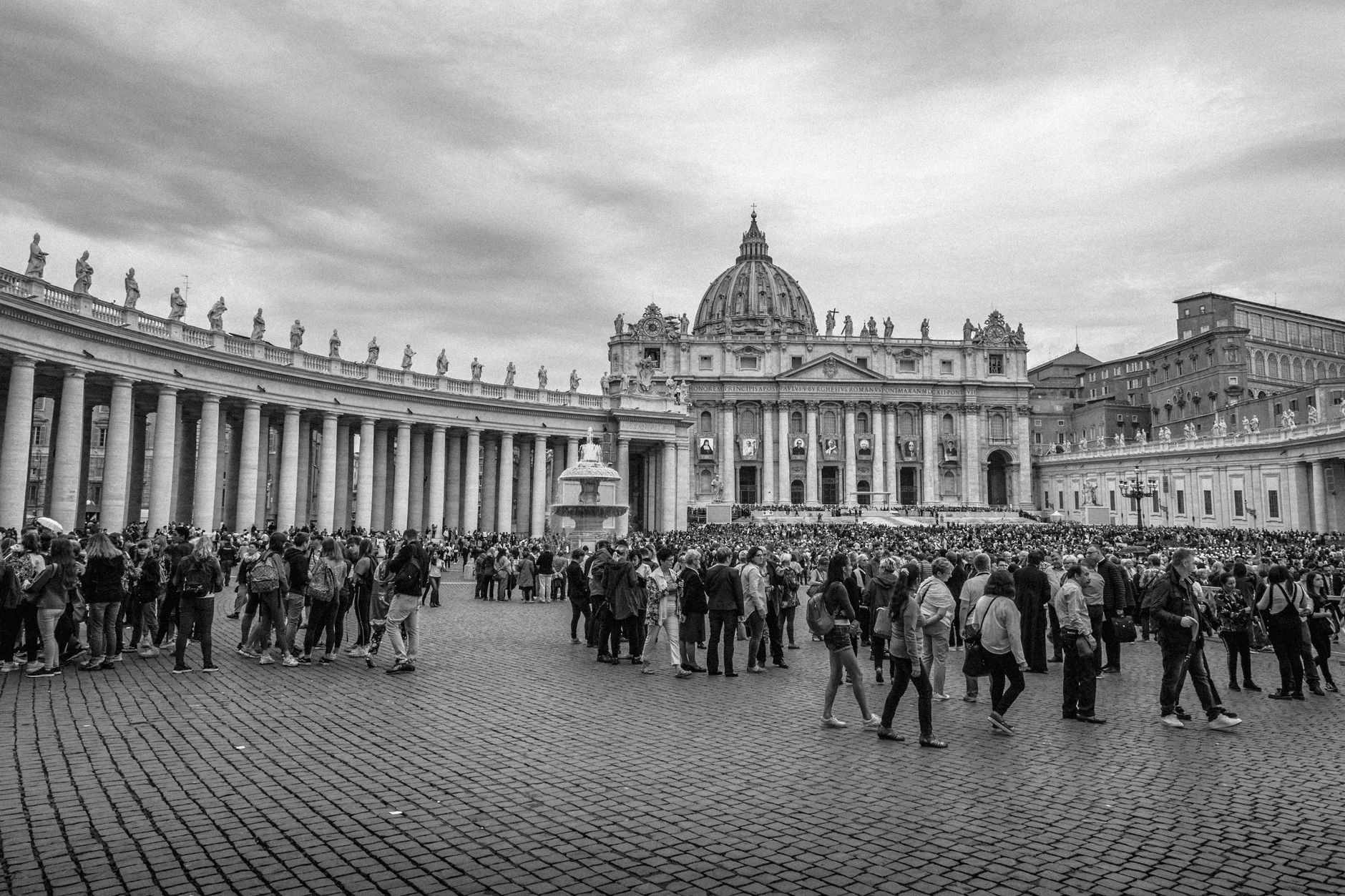 Grayscale image of a bustling crowd at Saint Peter's Square with Saint Peter's Basilica in view.