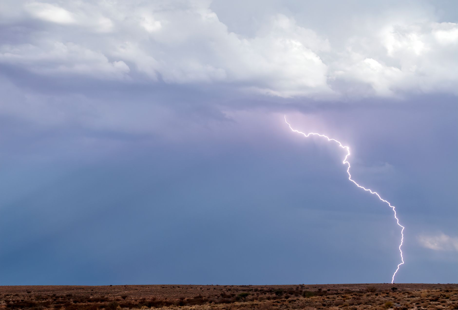 a vivid lightning bolt illuminating a stormy sky over desert terrain