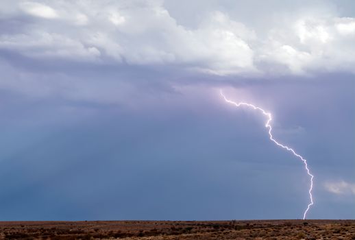 A vivid lightning bolt illuminates a stormy sky over a barren desert landscape, capturing nature's raw power.