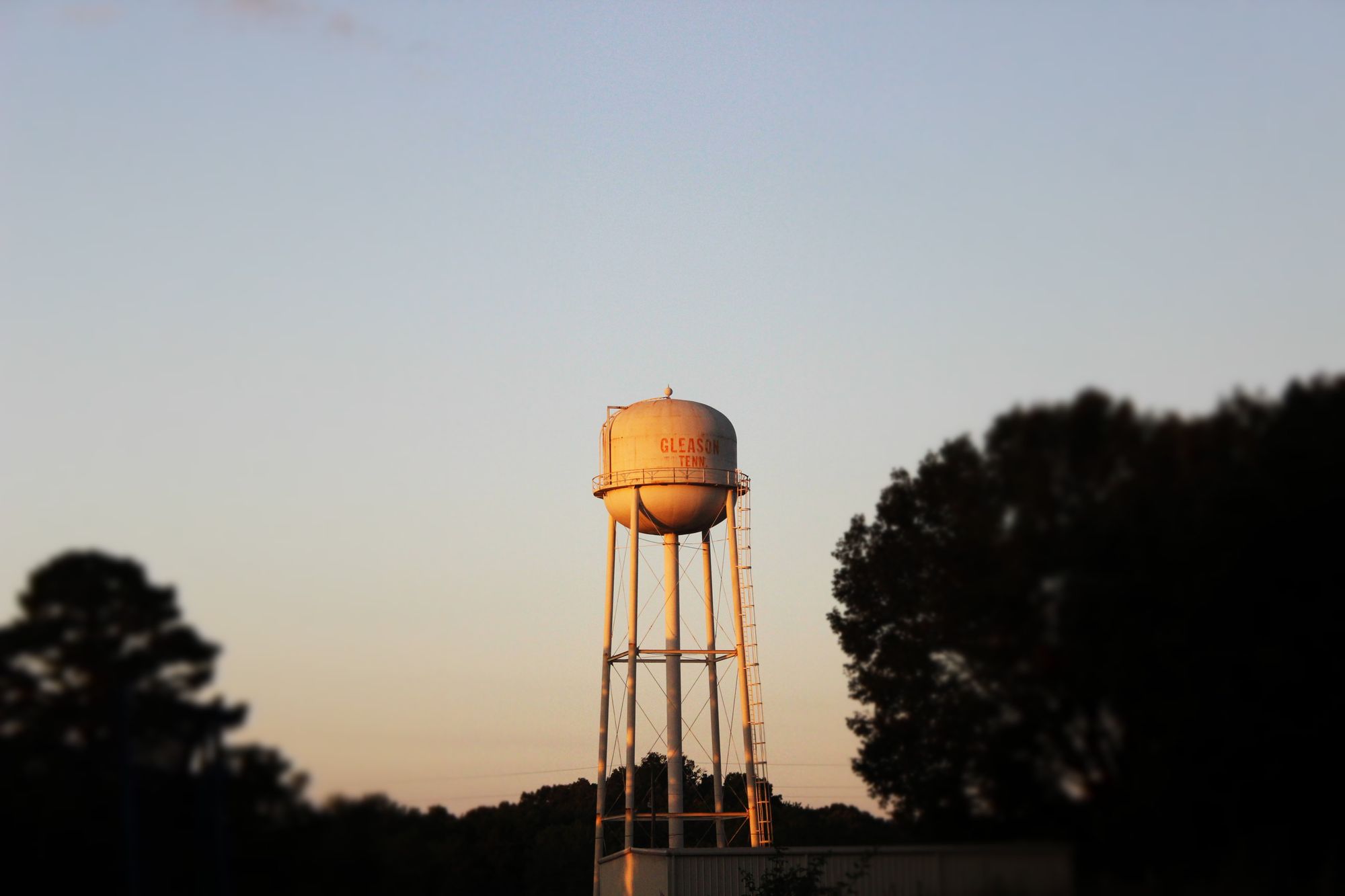 A water tower in Gleason, TN, surrounded by trees at sunset.