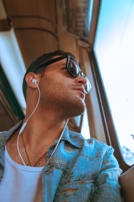 Fashionable man in sunglasses and earphones enjoying a metro ride on a sunny day.
