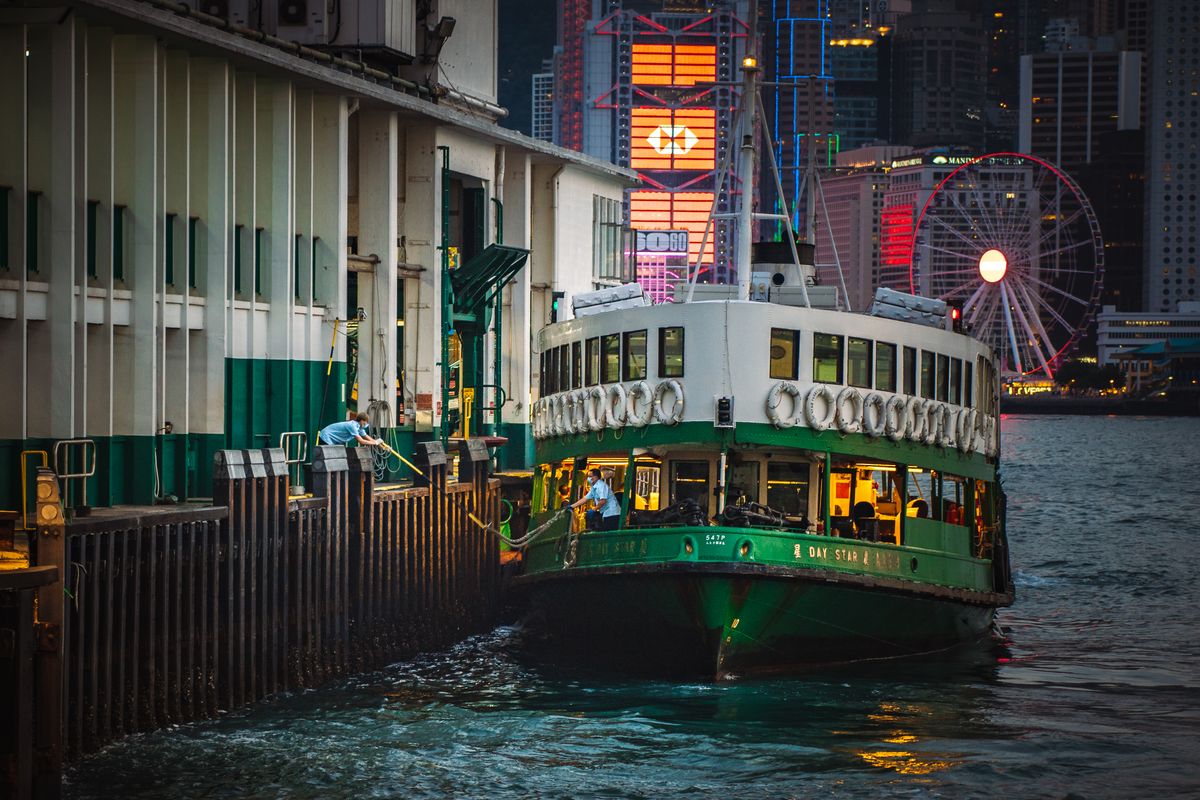 A Star Ferry docked at night with Hong Kong's illuminated skyline in the background