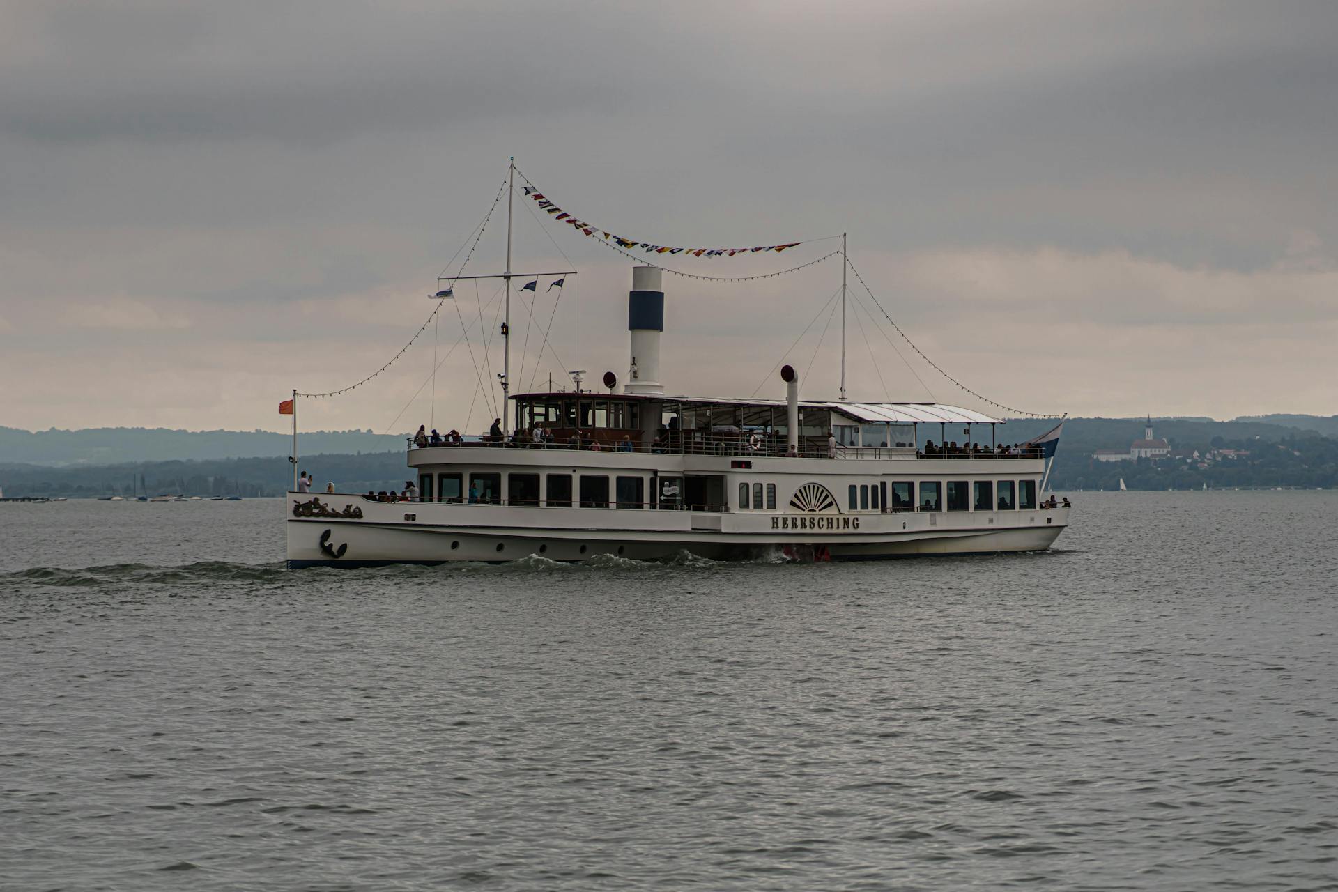 A vintage ferry boat crosses Ammersee, Germany under cloudy skies, offering a picturesque cruise experience.
