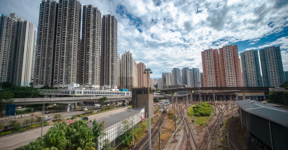 Dynamic cityscape of high-rise buildings and railways in Hong Kong under a partly cloudy sky.