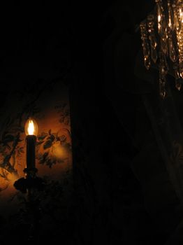 Moody candlelit scene with a gothic ambiance featuring a crystal chandelier and floral wallpaper.
