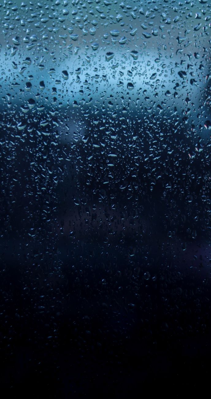 Close-up of water droplets on dark glass creating a moody, abstract texture.