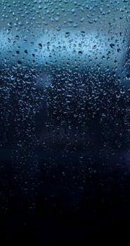 Close-up of water droplets on dark glass creating a moody, abstract texture.