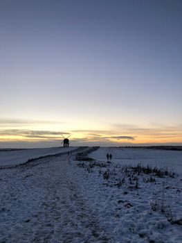 A serene winter landscape featuring a silhouette of a windmill against a colorful sunset sky.