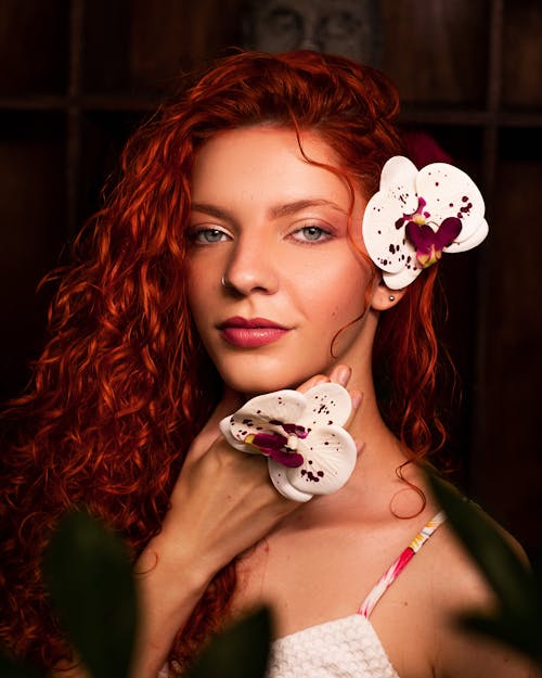 Beautiful Redhead Woman with Orchid Flowers in Hand and Hair 