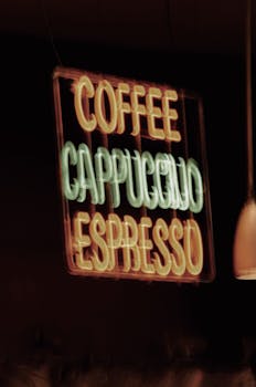 A blurred neon sign displaying coffee drinks like cappuccino and espresso.