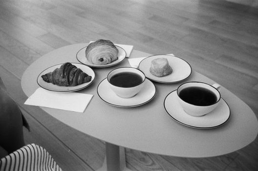Black and white photo of breakfast with coffee, croissants, and pastries on a table.