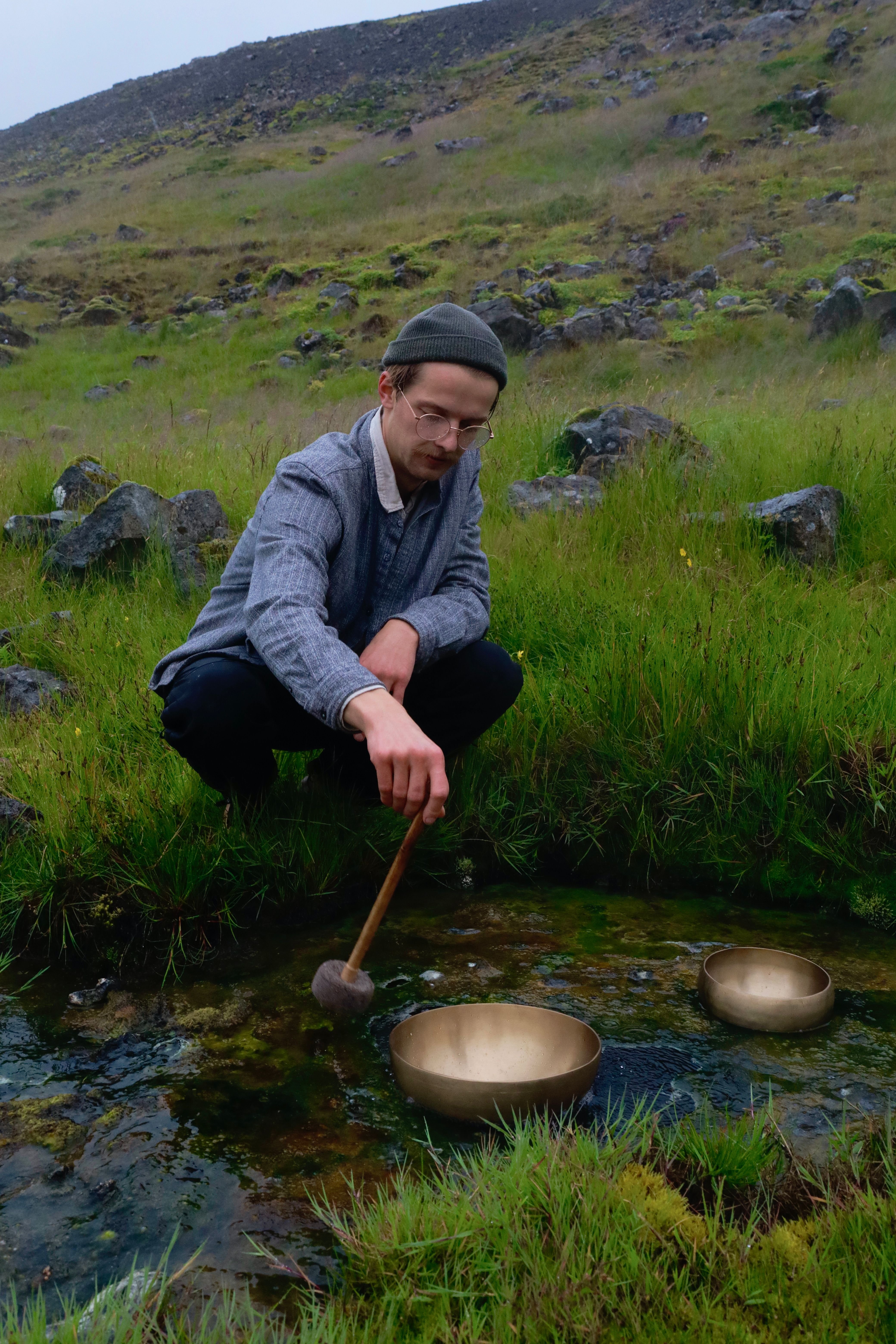 A man playing singing bowls in a serene Icelandic meadow.