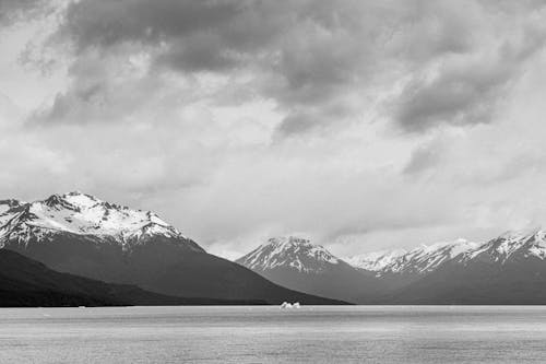 Grayscale Photo of Snowcapped Mountains Beside a Lake