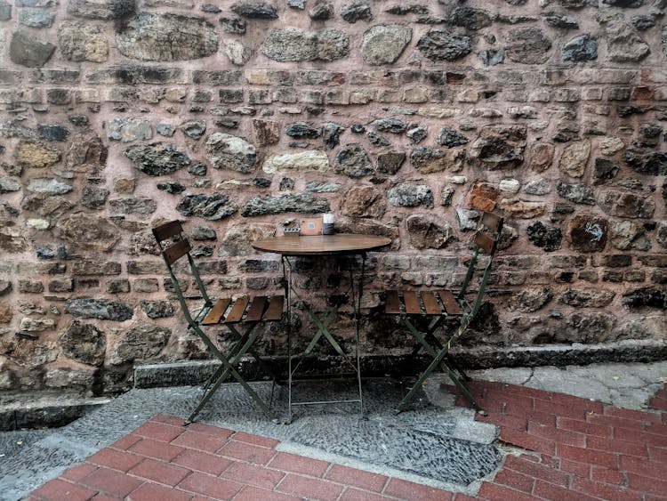 Brown Bistro Table With Chairs Beside Stone Wall