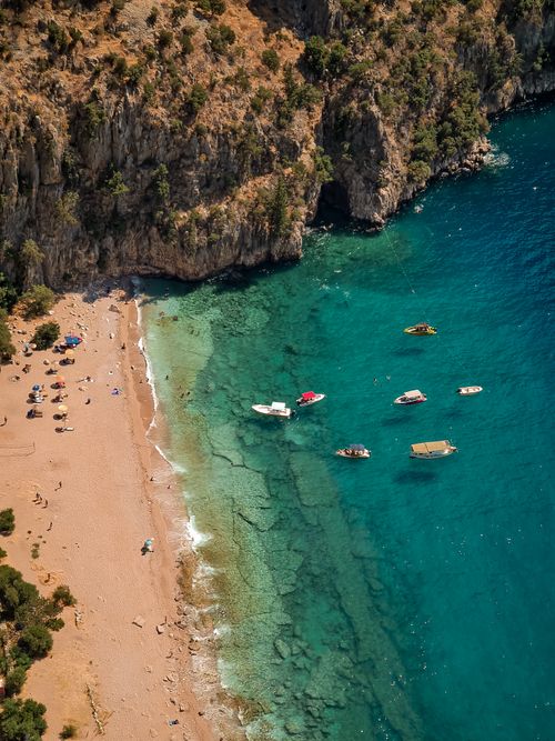 Free Aerial shot of a sandy beach by cliffs with boats on turquoise waters, perfect for summer vacation. Stock Photo
