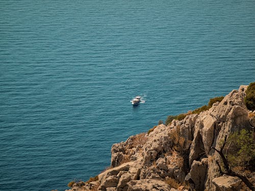 White and Black Boat on Ocean Water near Brown Rock Formation