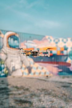 Close-up of a drone flying in front of colorful urban street art graffiti.