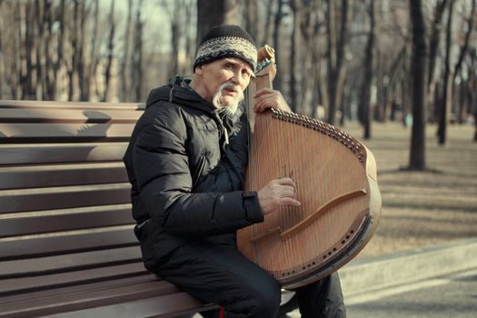 Elderly man enjoying music with a bandura on a park bench in Kharkiv.