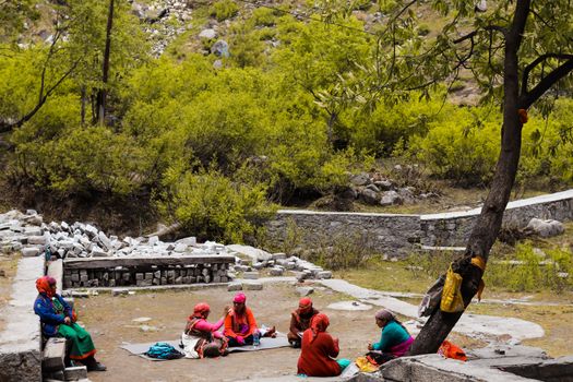 Group of women in colorful attire relaxing in a serene mountain landscape on a summer day.