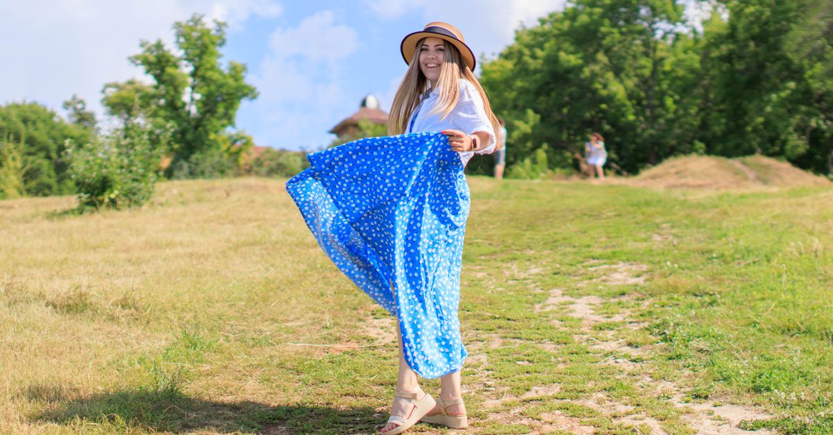 Smiling woman in a blue polka dot dress on a sunny day outdoors.