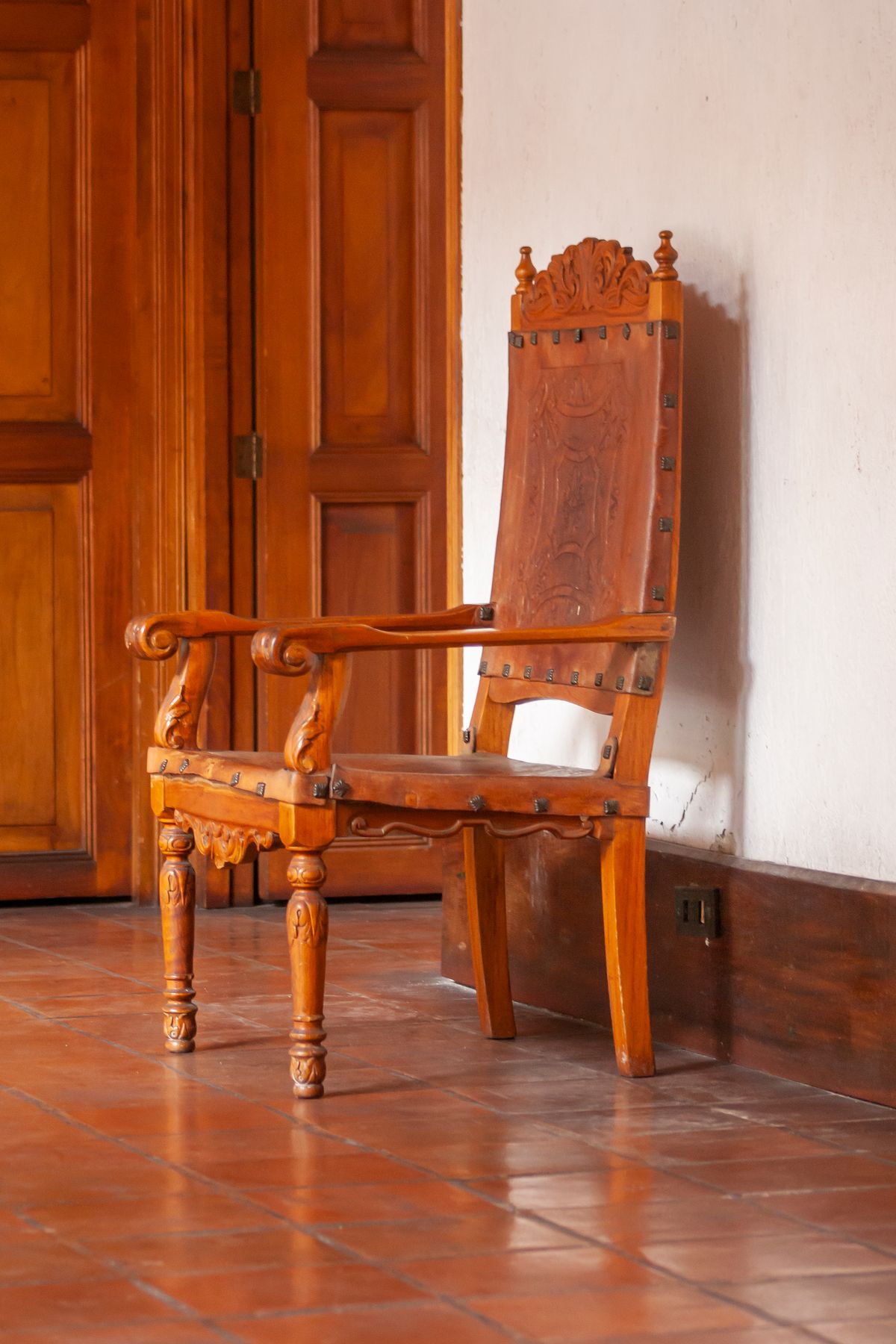 Tall carved armchair with leather upholstery beside a wooden door