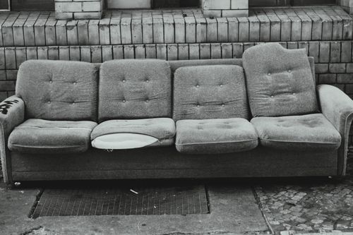 Free A grayscale image of an abandoned torn sofa against a brick wall in Berlin. Stock Photo
