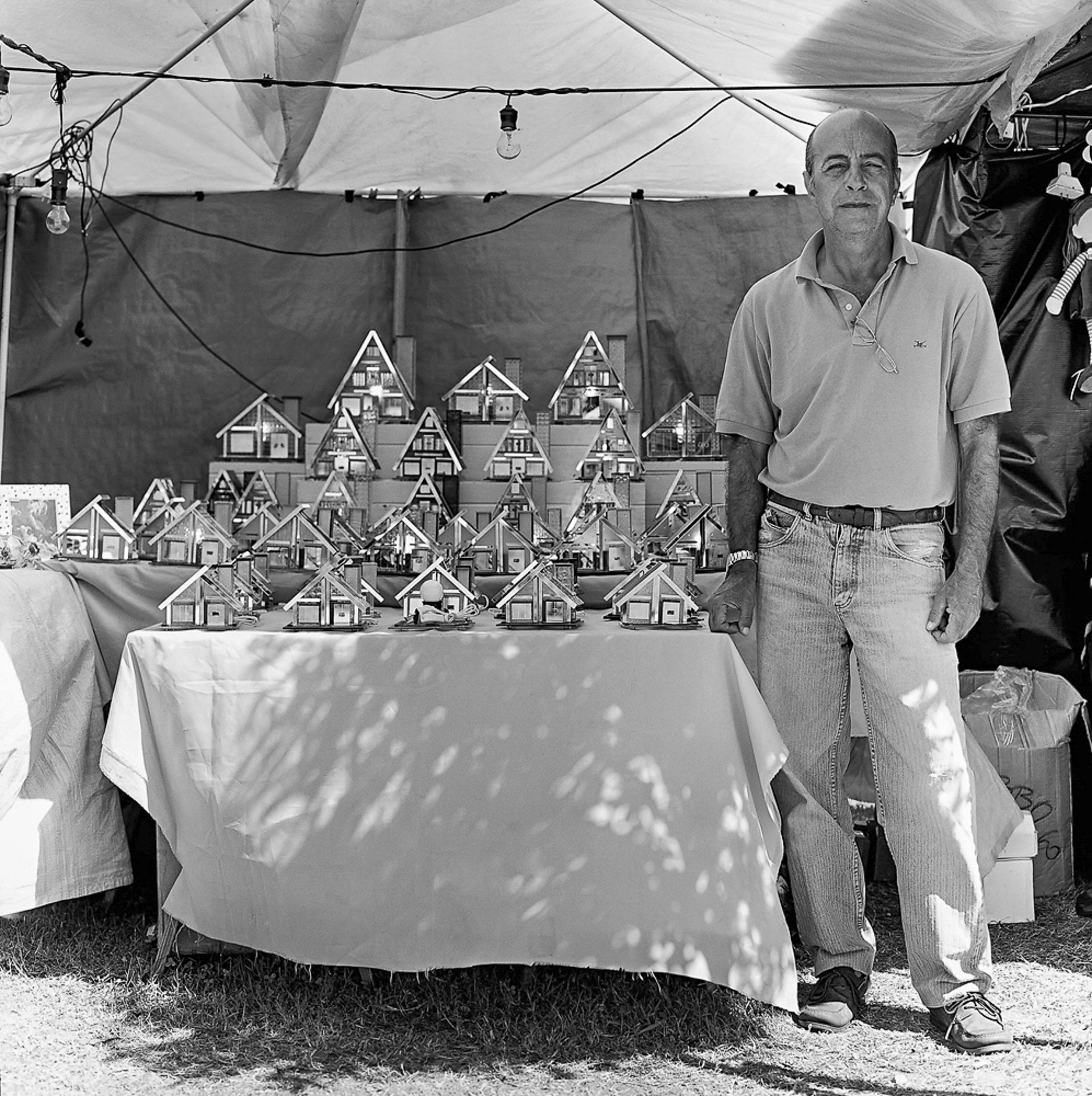 Man stands at market stall displaying miniature houses in Buenos Aires, Argentina.