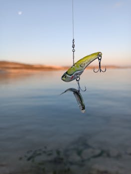 Vibrant fishing lure with a small fish in a serene river setting at dawn.