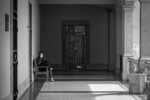 Free A black and white photo of a woman wearing a face mask sitting alone in a hallway. Stock Photo