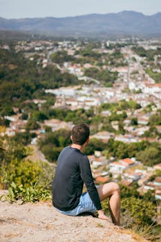 A man sitting on a hillside looks over a scenic Brazilian town during a warm summer day.