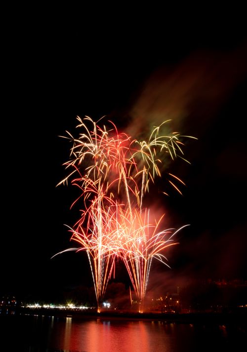 Free Spectacular fireworks illuminating the night sky over a water body, creating reflections with colorful bursts. Stock Photo