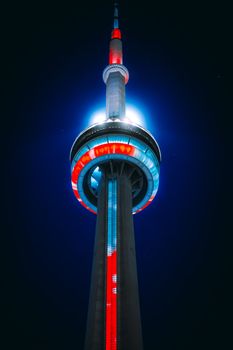 Dramatic night view of the iconic illuminated CN Tower in Toronto with vibrant red and blue lights.