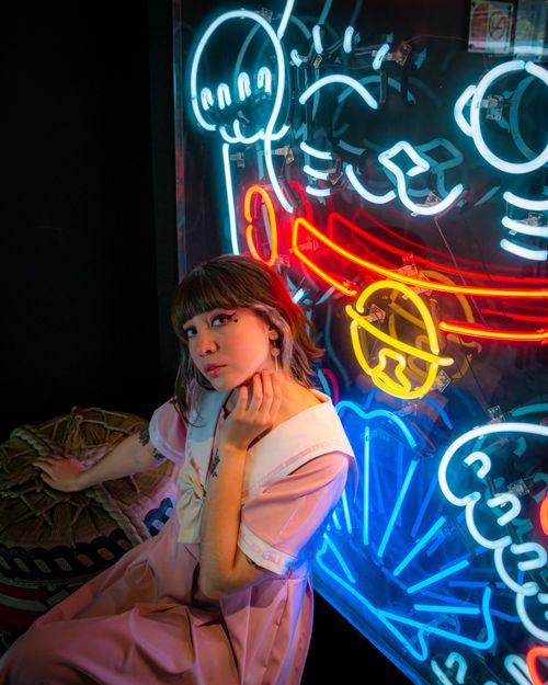 Free A young woman poses in front of a colorful neon art display, creating a vibrant and modern ambiance. Stock Photo
