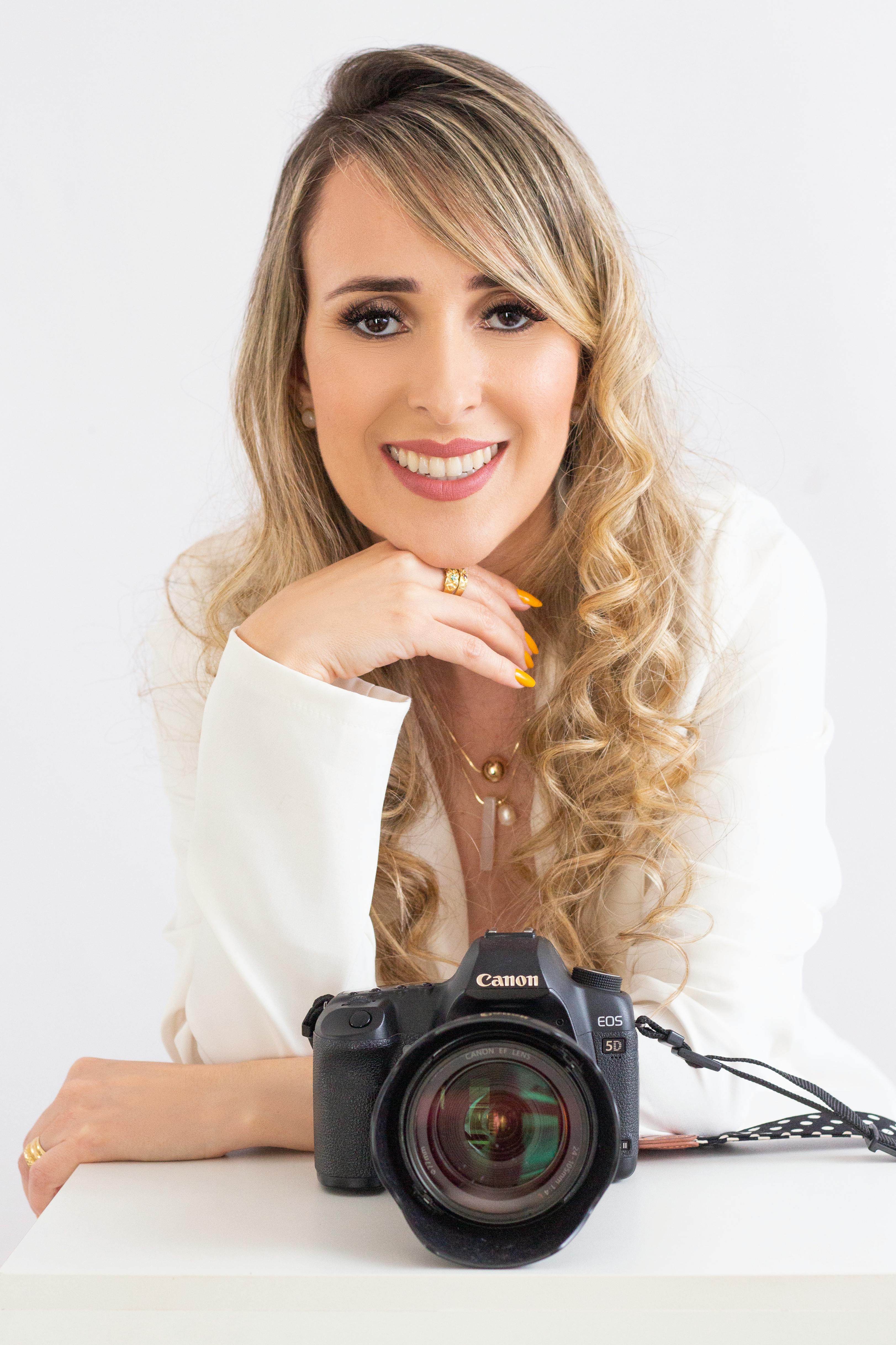 Smiling woman with curly blonde hair and camera in a studio setting.
