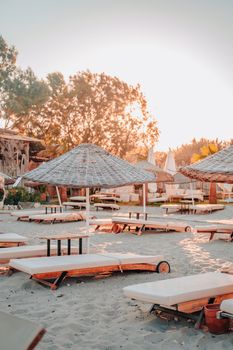 Peaceful beach scene at sunset featuring loungers under umbrellas and warm sunlight.