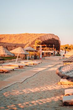 A stunning tropical beach scene with a wooden pathway leading to a resort bar under a clear blue sky.