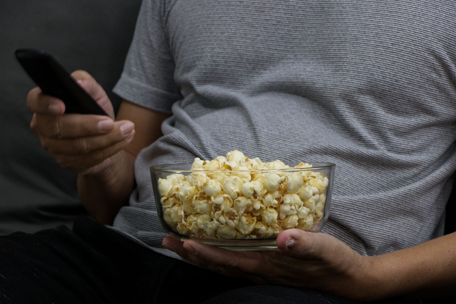 Person holding a bowl of popcorn and remote, capturing a cozy movie night vibe. Person holding a bowl of popcorn and remote, capturing a cozy movie night vibe.