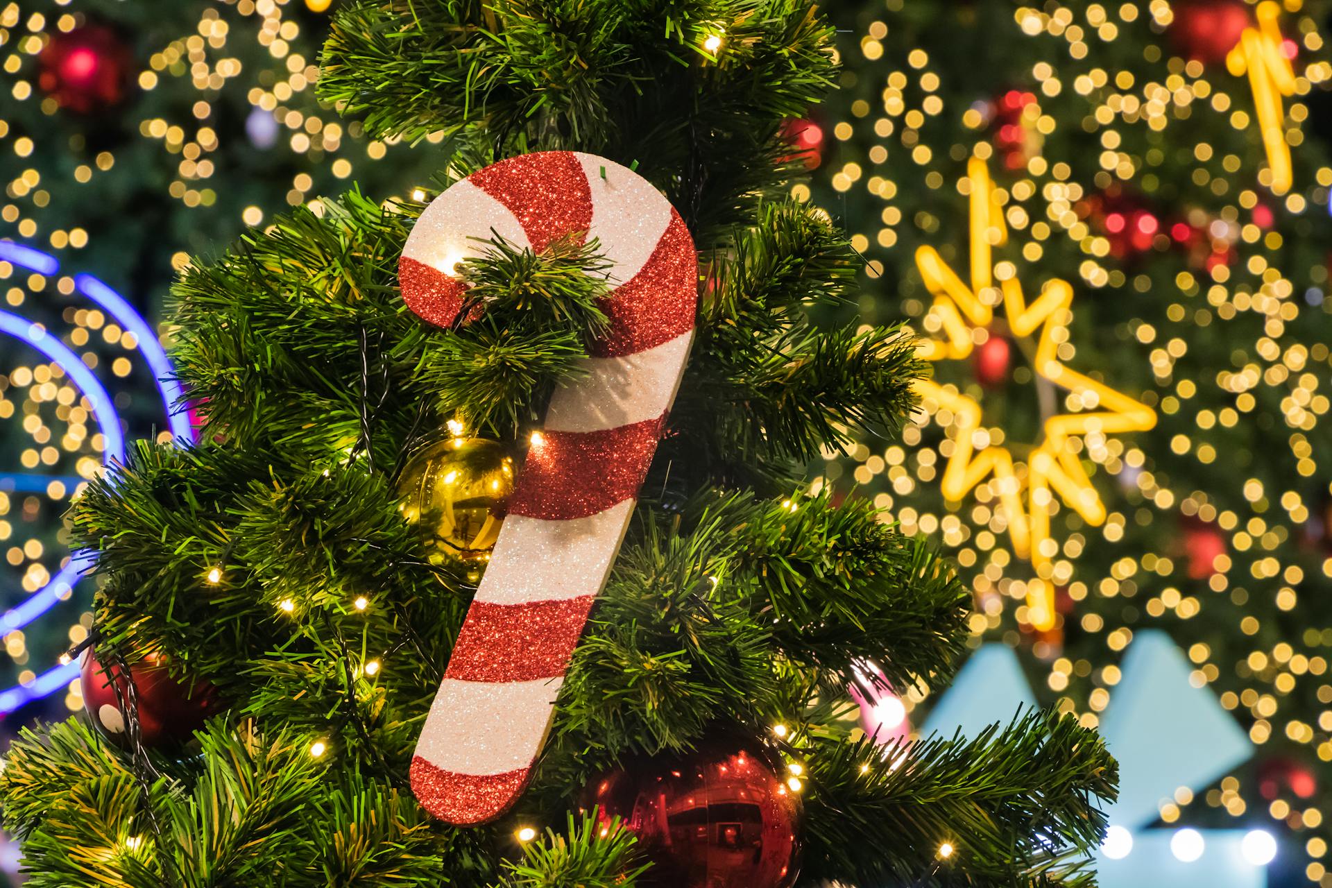 Close-up of a Christmas tree adorned with a glittery candy cane ornament and bokeh lights in the background.