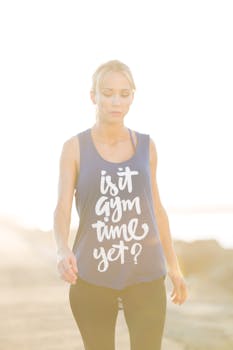 A young woman in fitness gear enjoys the outdoors, wearing a stylish tank with 'Is It Gym Time Yet?' text.
