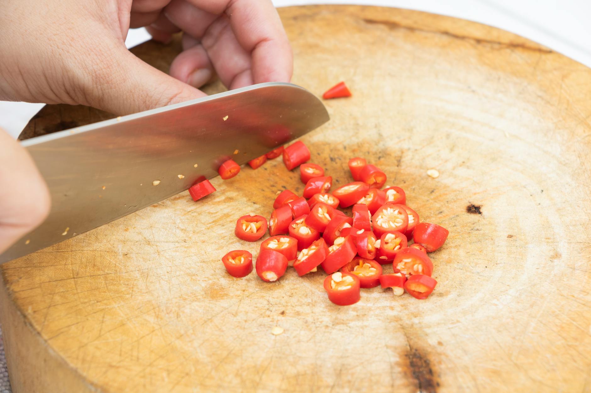 Person slicing fresh red chili peppers on a wooden chopping board.