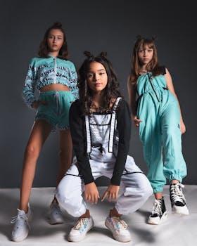 Three teenage girls in fashionable outfits striking confident poses against a gray backdrop.