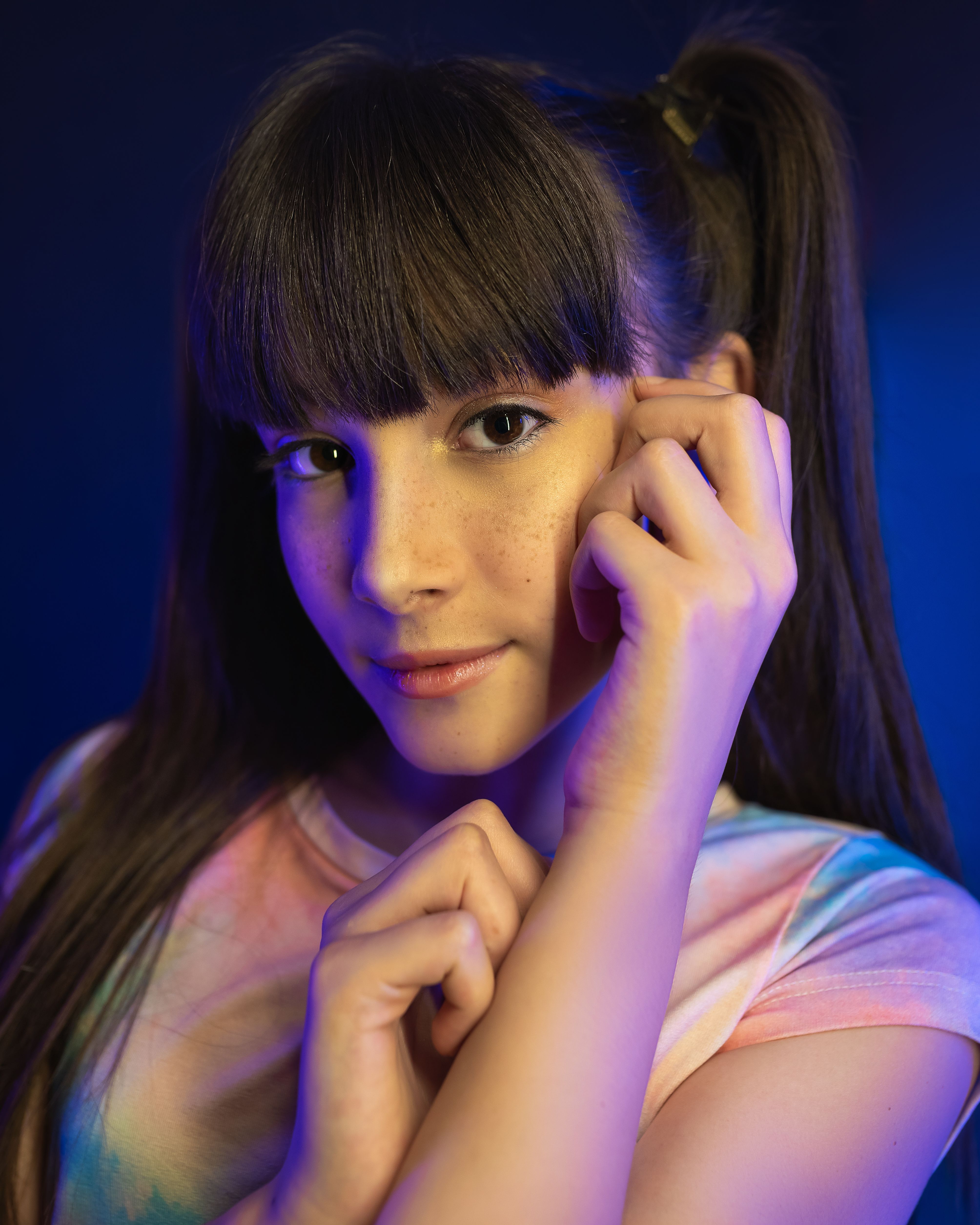 Close-up portrait of a young woman with bangs under colorful studio lighting, showcasing elegance and youth.