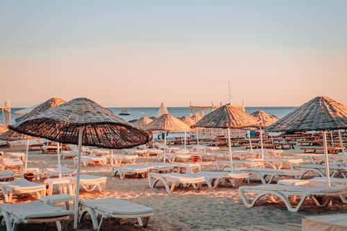 Free A serene beach scene with lounge chairs and umbrellas at sunset, ideal for vacation vibes. Stock Photo