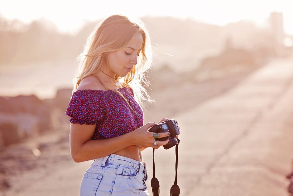 A young woman capturing photos during a serene summer sunset outdoors.