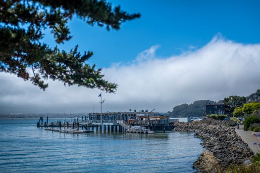 A picturesque view of a coastal pier with fog drifting over the nearby hills and tranquil waters.