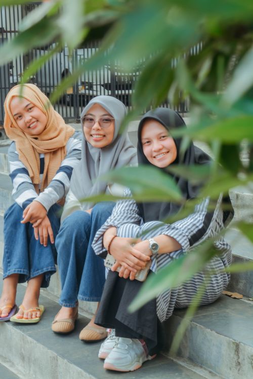 Free Three smiling friends with hijabs sitting outdoor steps, symbolizing friendship and diversity. Stock Photo