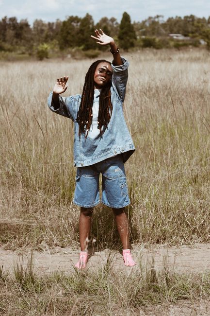 A woman in a denim jacket stands joyfully in a grass field, capturing freedom and leisure.