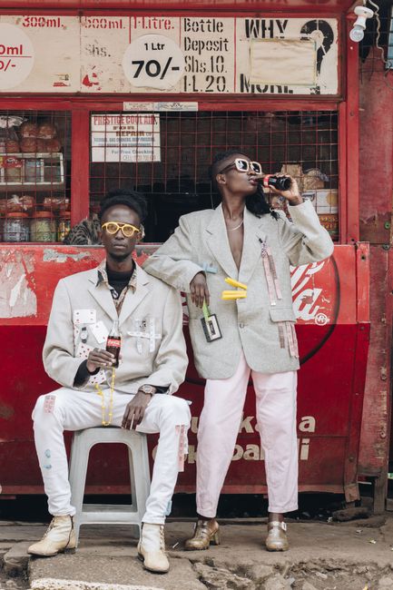 Two fashionably dressed individuals enjoy soda outside a vibrant shop.