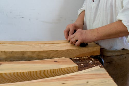 A Person in White Long Sleeve Shirt Scraping Wood Plank